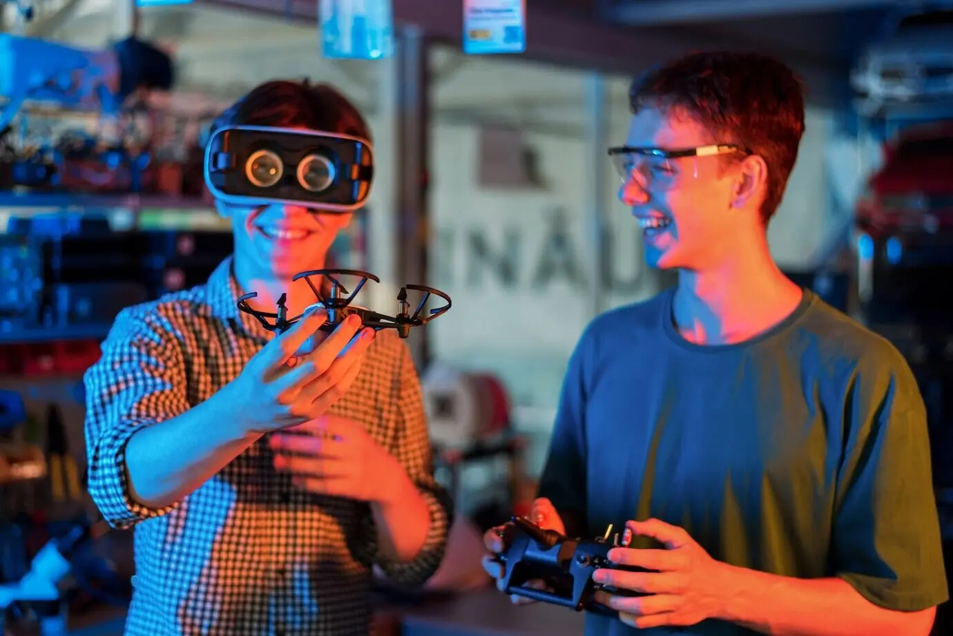 Lächelnde Teenager führen in einem Labor Robotik-Experimente durch; ein Junge mit VR-Headset hält eine kleine Drohne.