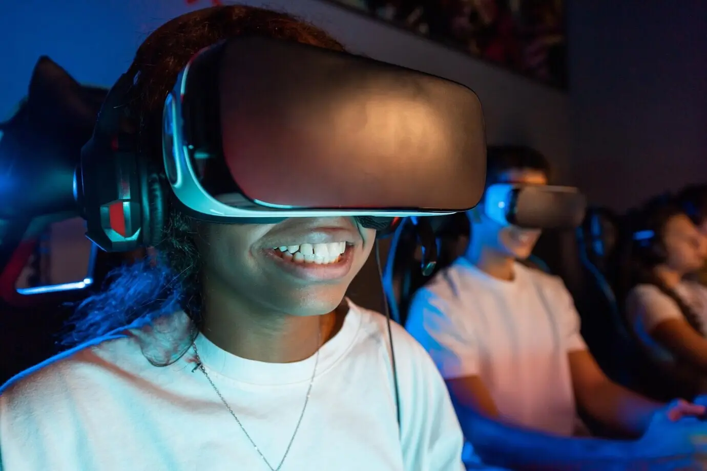 Lächelnde schwarze Teenagerin mit VR-Headset spielt Videospiele in einem Videospielclub mit blauer Beleuchtung.